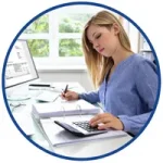 Kurs podatkowy dla samodzielnych księgowych – kobieta notuje przy biurku z kalkulatorem, segregatorem i monitorem