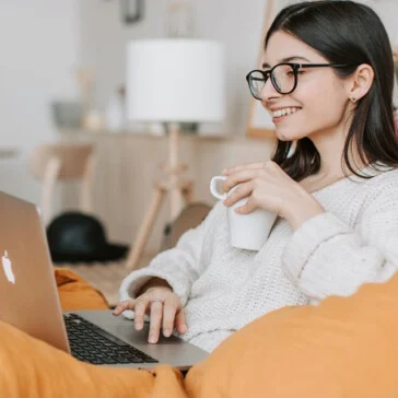 Jak praca zdalna będzie uregulowana od 2023 roku – kobieta z kubkiem pisze na laptopie na kanapie w domu