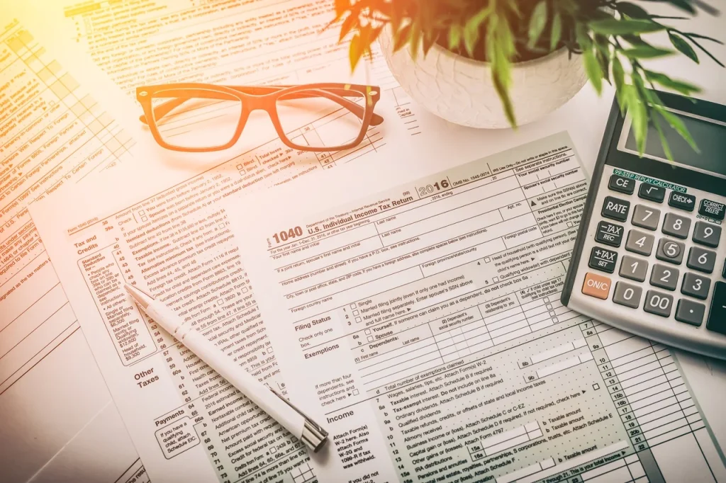 Jakie zmiany czekają przedsiębiorców w 2025 r. – formularze podatkowe, okulary, długopis i kalkulator na biurku