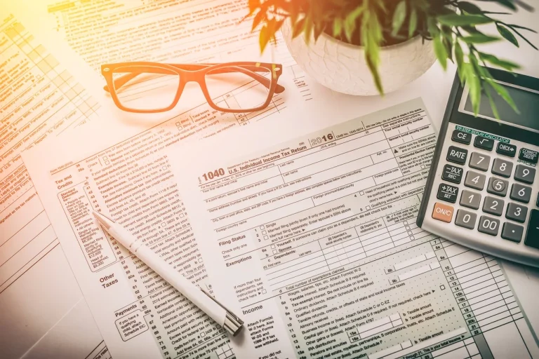 Jakie zmiany czekają przedsiębiorców w 2025 r. – formularze podatkowe, okulary, długopis i kalkulator na biurku