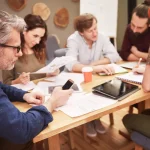 Kurs rachunkowości budżetowej dla JST – pięć osób pracuje przy stole nad wydrukami z wykresami i tabletem