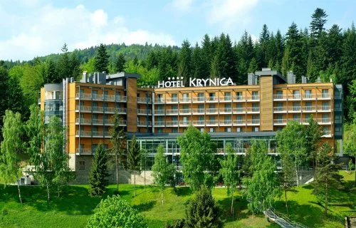 Szkolenia wyjazdowe w Krynicy-Zdroju – czterogwiazdkowy hotel z napisem „Hotel Krynica” na zboczu wśród świerków