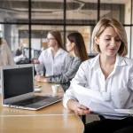 Bezpłatne webinary kadrowe dla sektora publicznego – kobieta przegląda dokumenty przy stole z laptopem w biurze
