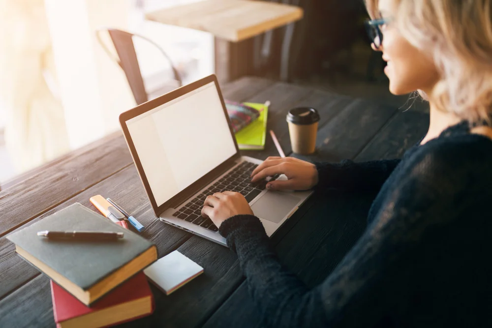 Kursy z kompetencji cyfrowych i nowych technologii – kobieta pisze na laptopie przy stole z książkami