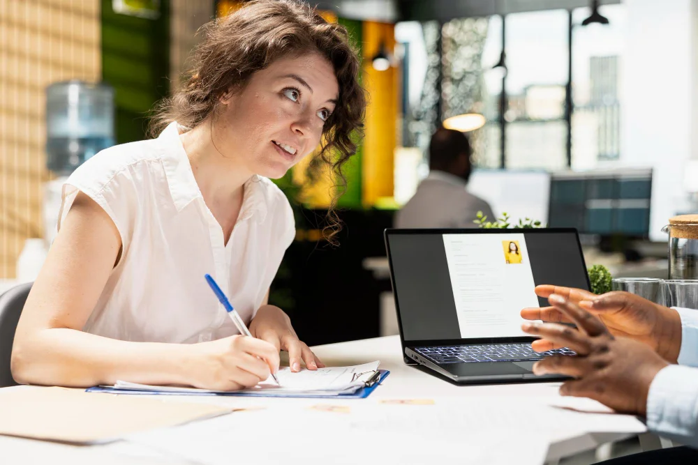 Kursy MS Office – uczestniczka notuje na podkładce podczas konsultacji przy laptopie z otwartym dokumentem