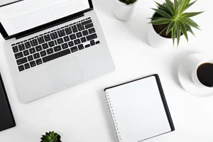 biurko z góry: laptop, notes, kawa, rośliny — też bez ludzi