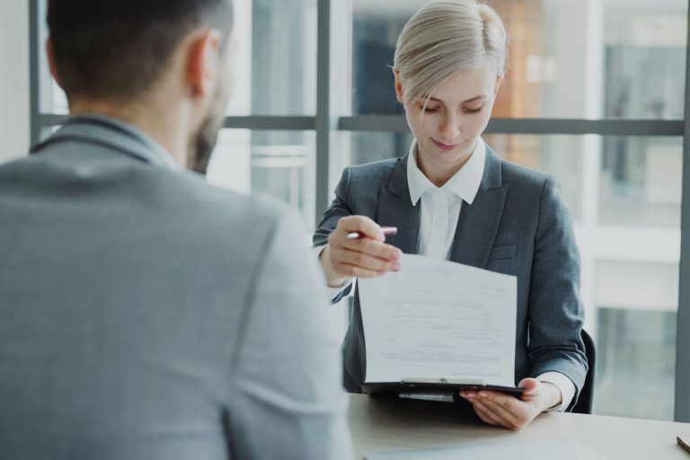 Specjalistka ds. kadr podaje pracownikowi dokument do zapoznania się w biurowej sali spotkań. Zdjęcie ilustruje obowiązek poinformowania pracowników o zmianie regulaminu pracy lub wynagradzania.